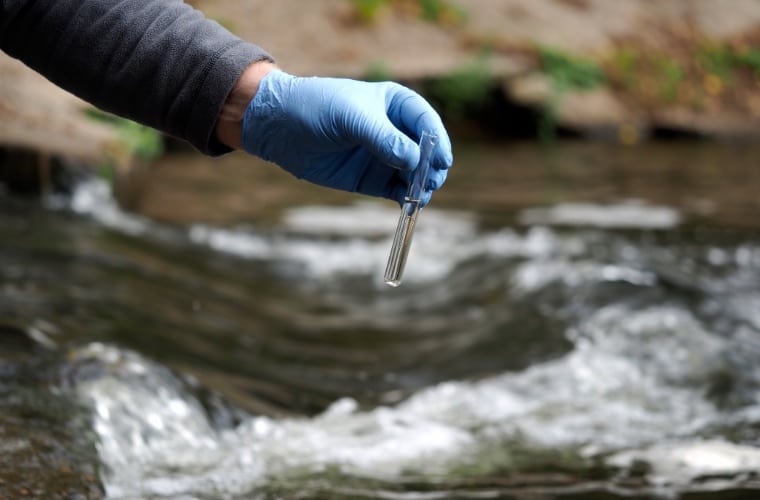 scientist uses tube to collect water samples from river
